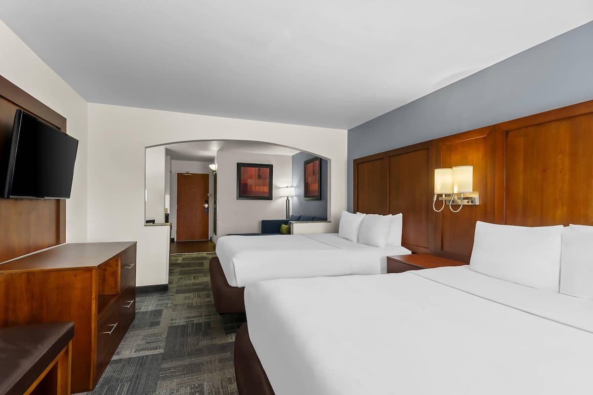 A hotel room with two beds, a TV, a desk, and a bathroom visible through an archway.