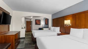 Une chambre d’hôtel avec deux lits, une télévision, un bureau et une salle de bain visible à travers une arche.