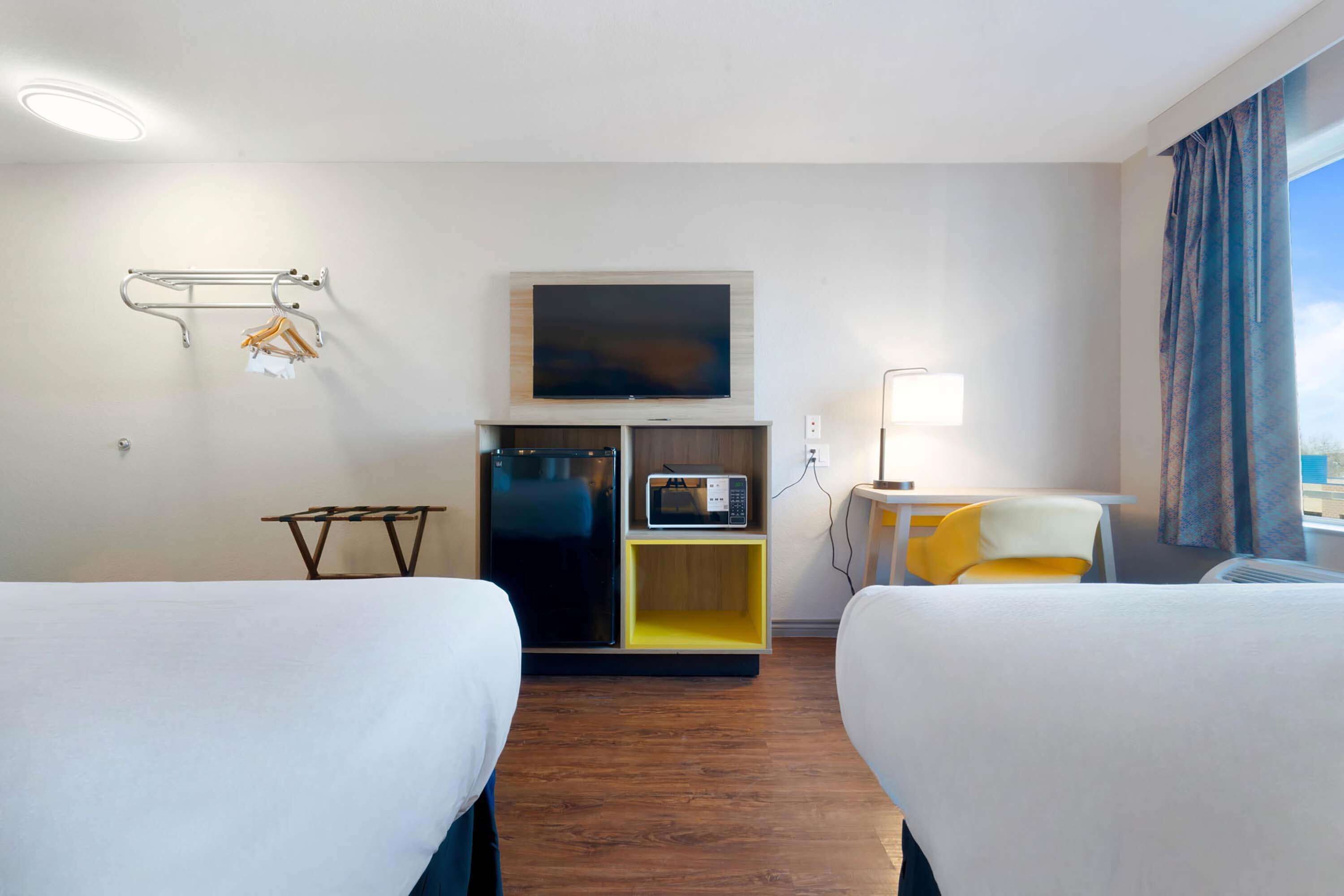 A hotel room with two beds, a TV, a microwave, and a small table with a lamp.