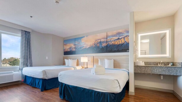 A hotel room with two beds, a large mountain landscape painting, a bathroom with a vanity and mirror, and a window with curtains. - Days Inn by Wyndham Thornton (Thornton)