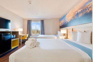 Habitación de hotel con una cama grande, un escritorio, un televisor y un cuadro de un paisaje montañoso.