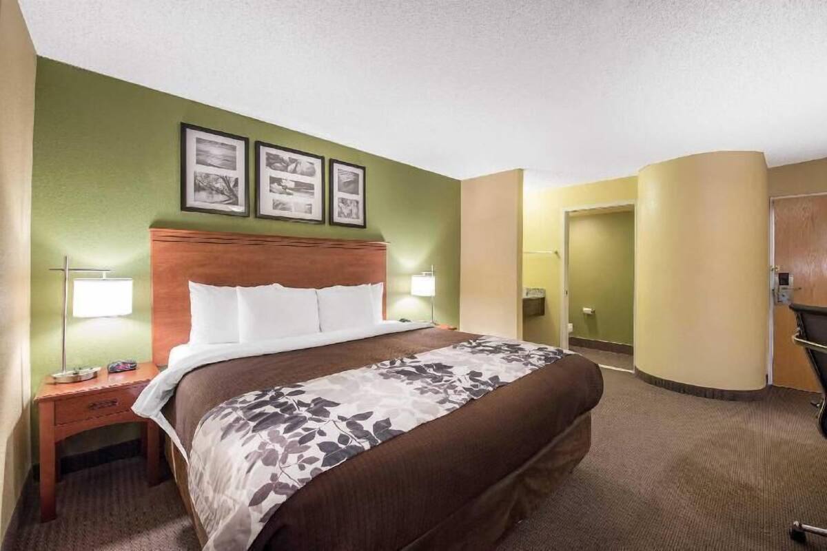 A hotel room with a bed, nightstand, lamp, and framed pictures on the wall.