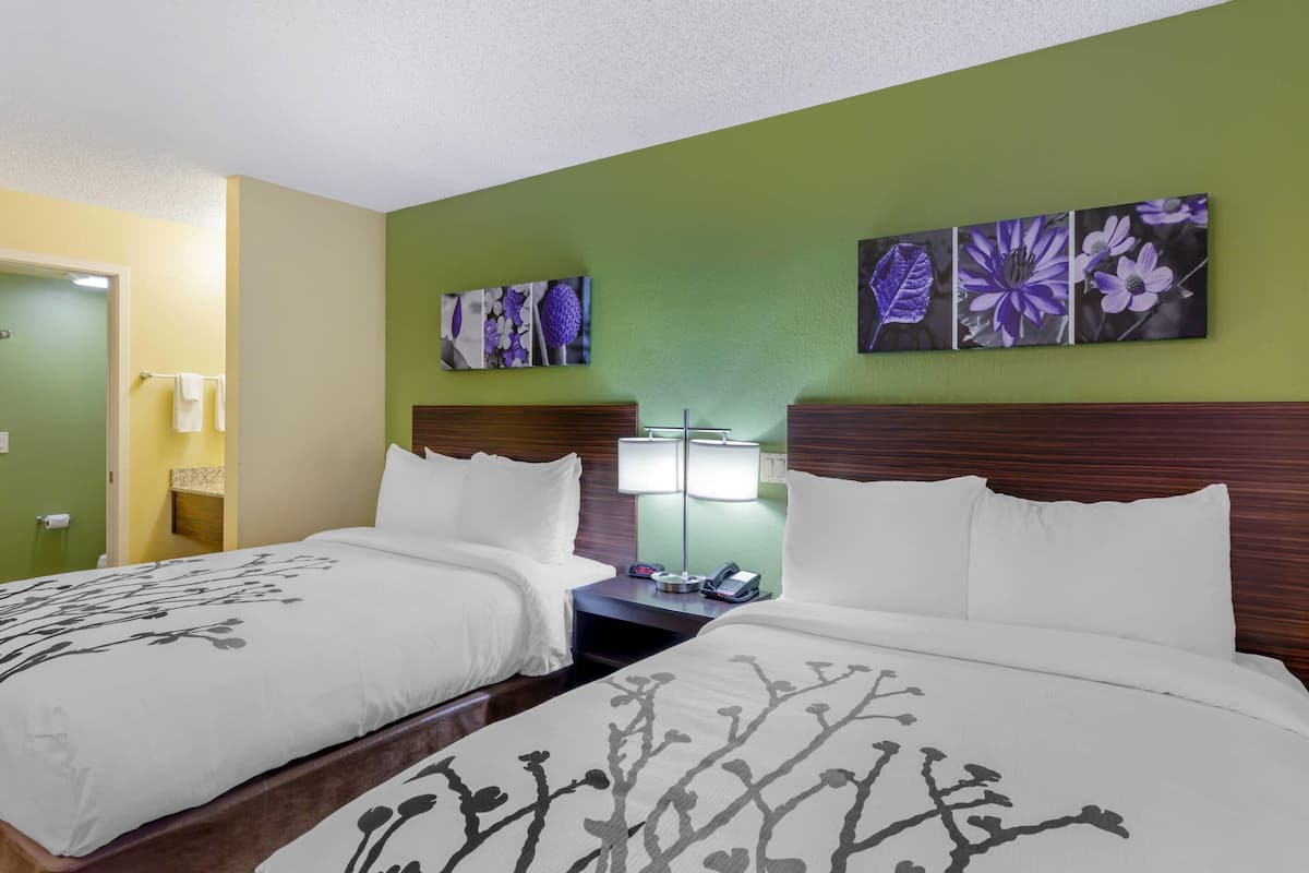 A hotel room with two beds, a nightstand with a lamp, and artwork on the wall.