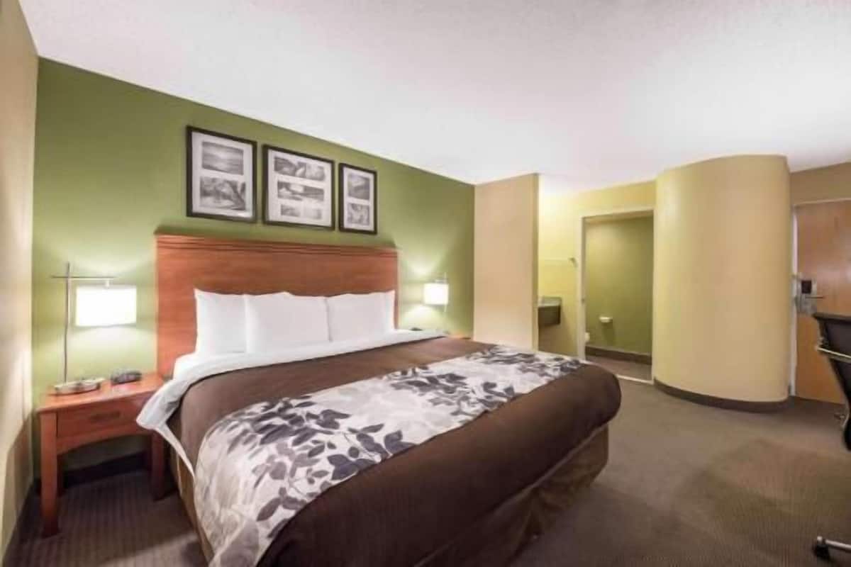A hotel room with a bed, a nightstand, a lamp, and a door.