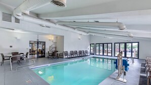 A large indoor swimming pool with clear blue water, surrounded by seating areas and a view of the outdoors through large windows. - Sleep Inn Denver Tech Center (Greenwood Village)