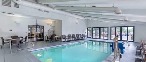 A large indoor swimming pool with clear blue water, surrounded by seating areas and a view of the outdoors through large windows.