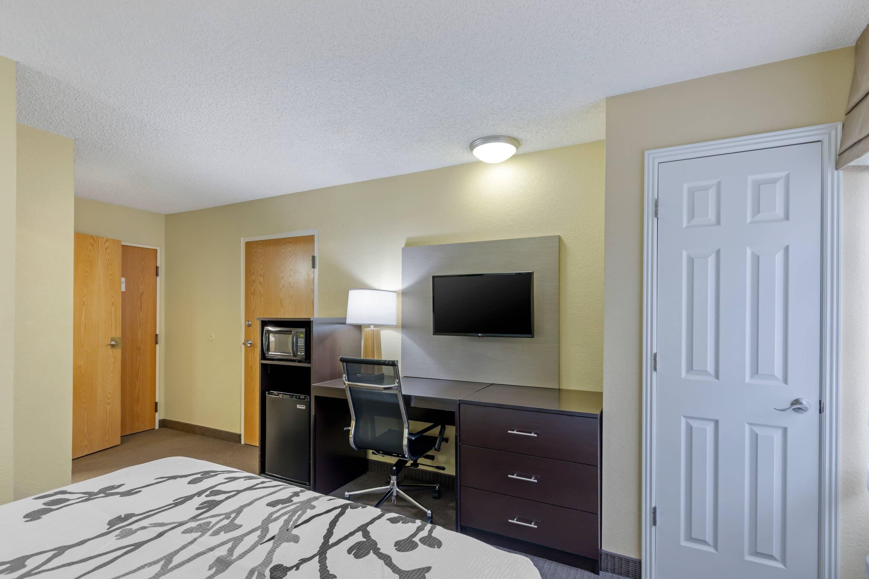 Habitación de hotel con cama, escritorio, silla, televisión, microondas y puerta.
