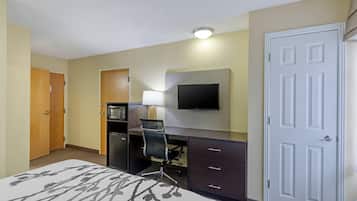 Habitación de hotel con cama, escritorio, silla, televisión, microondas y puerta.