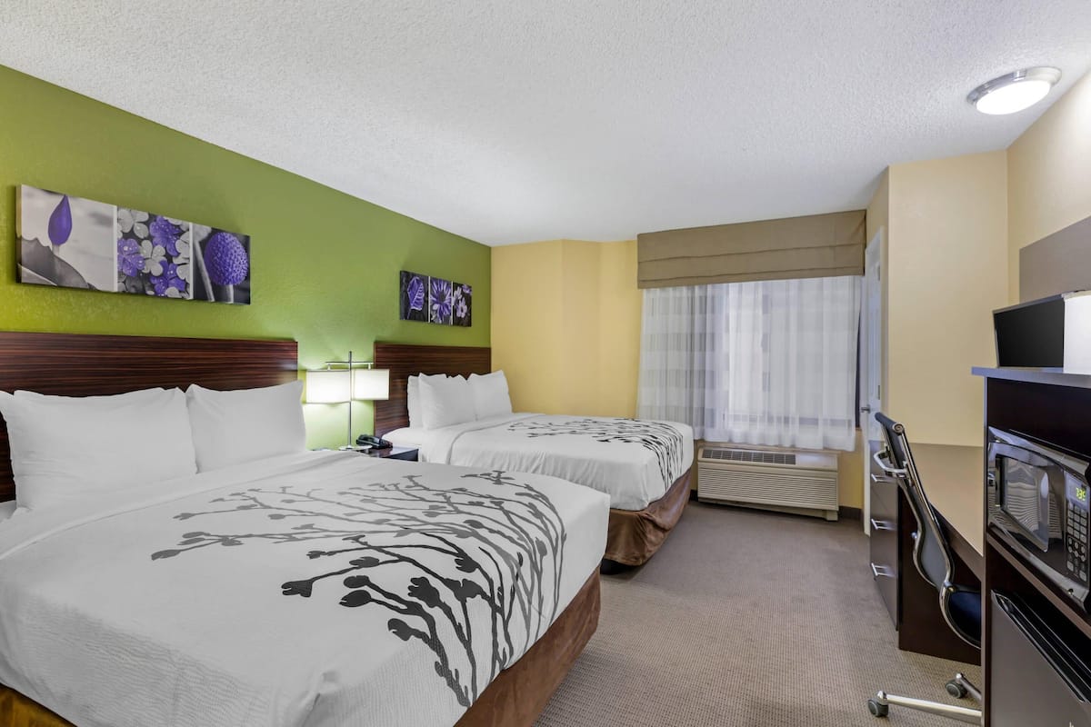 A hotel room with two beds, a desk with a computer, a TV, and artwork on the walls.