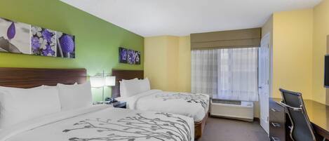 A hotel room with two beds, a desk, a chair, a television, and artwork on the walls.