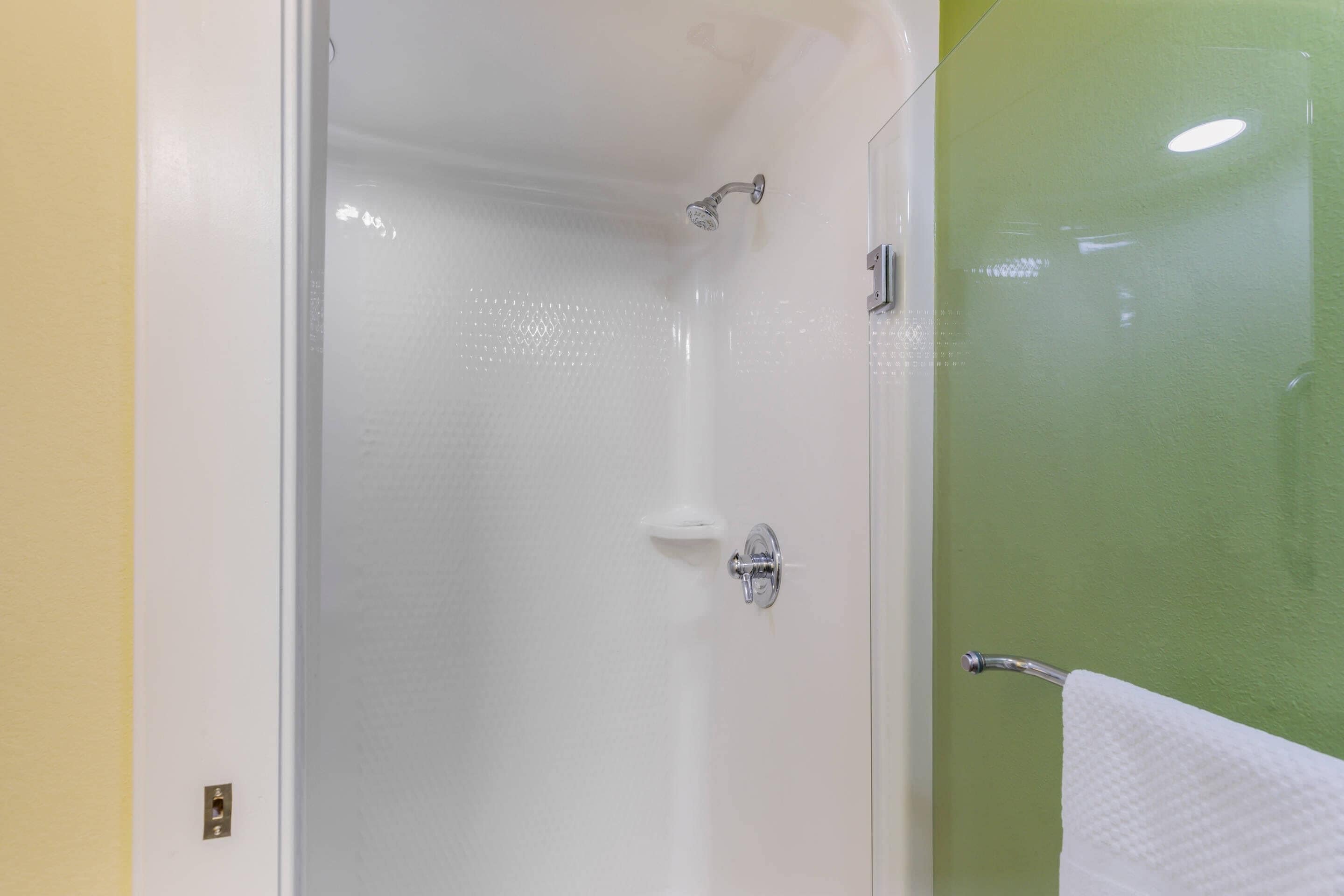 Ducha envuelta en vidrio con cabezal de ducha de mano y controles en la pared.