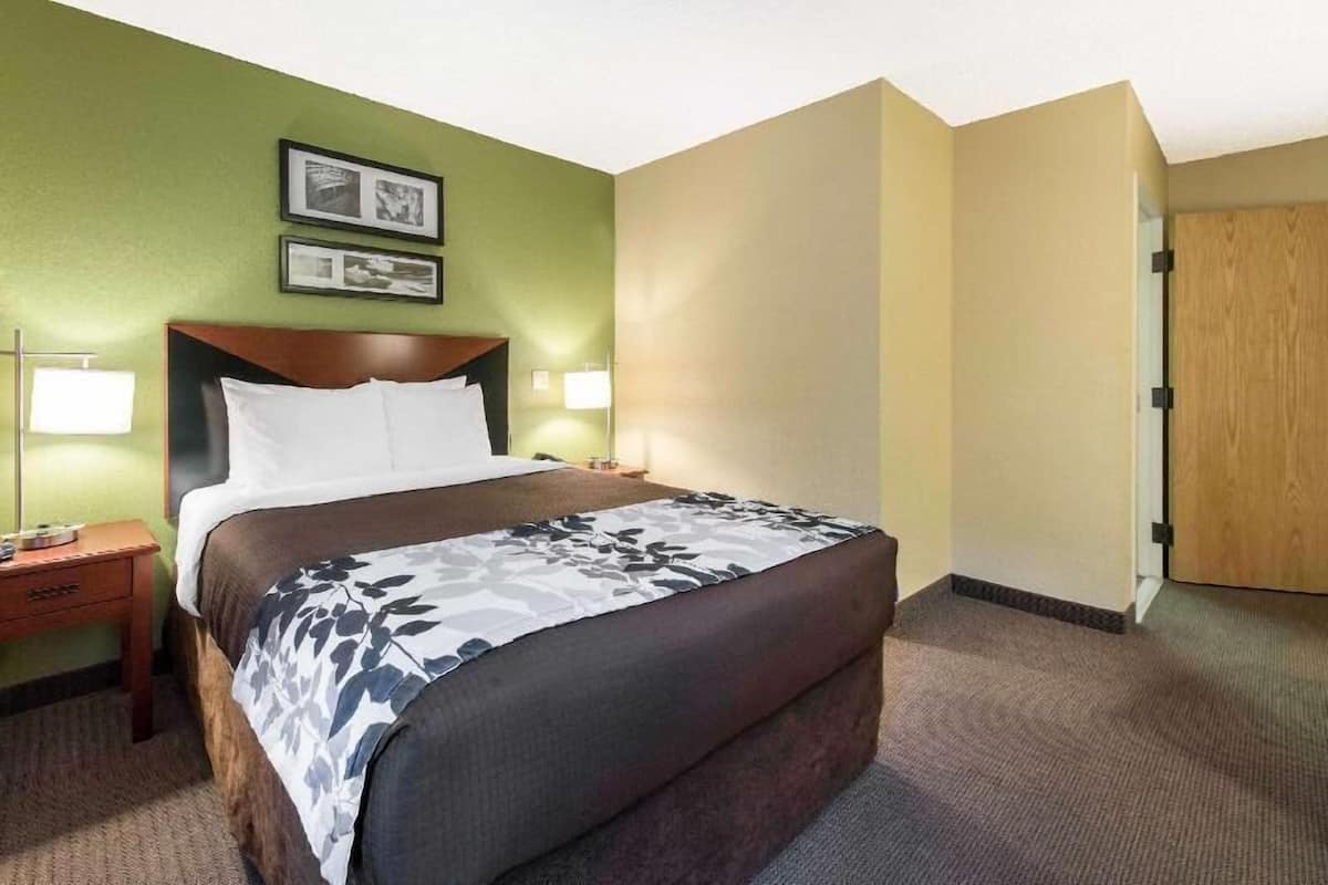 A hotel room with a bed, bedside lamps, a nightstand, and a door.