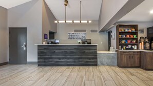 Un espace d’accueil avec un comptoir de réception en bois foncé, deux ordinateurs, un coin café et une étagère à collations.