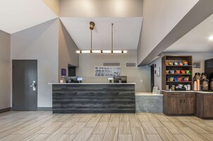 Un área de recepción con un mostrador de madera oscura, dos computadoras, una estación de café y un estante con aperitivos.