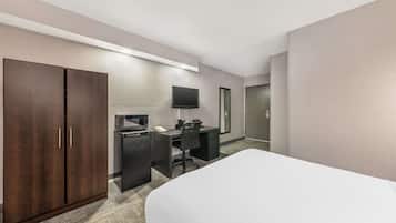 Una habitación de hotel con una cama, un escritorio con computadora, un televisor y un armario.