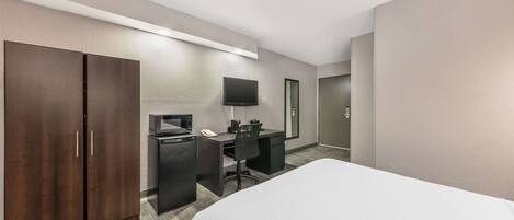 A hotel room with a bed, a desk with a computer, a TV, and a wardrobe.