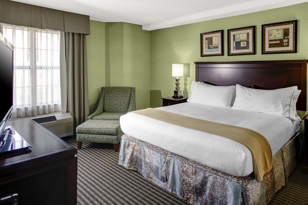 A hotel room with a large bed, a desk with a computer, a chair, a lamp, and framed pictures on the wall.