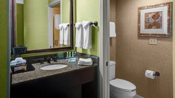 A bathroom with a sink, mirror, towel rack, toilet, and a framed picture on the wall.