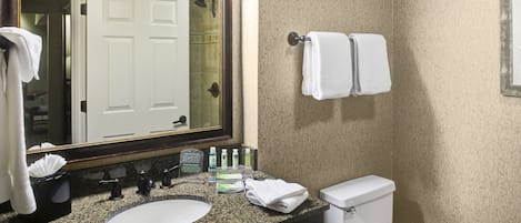 A bathroom with a granite countertop, a sink, a mirror, a toilet, and two towels hanging on a towel rack.
