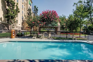 A swimming pool with lounge chairs and a covered seating area, surrounded by a fence and trees. - Holiday Inn Express & Suites Atlanta Buckhead by IHG (Atlanta)