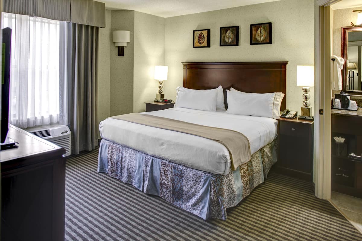 A hotel room with a large bed, two bedside tables with lamps, a desk, and a wardrobe.