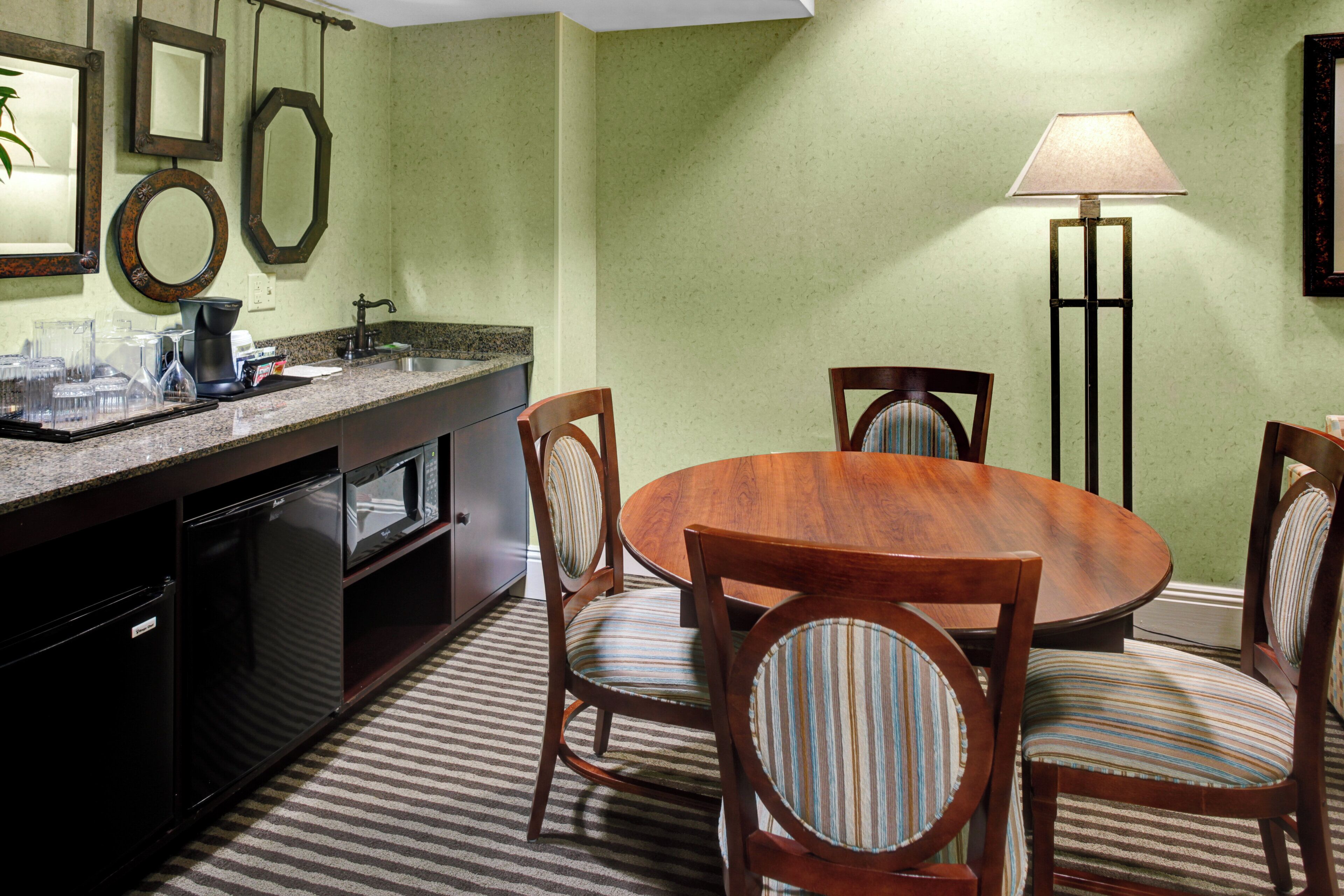 A dining area with a round wooden table and four chairs, a kitchen with a granite countertop, and a floor lamp.