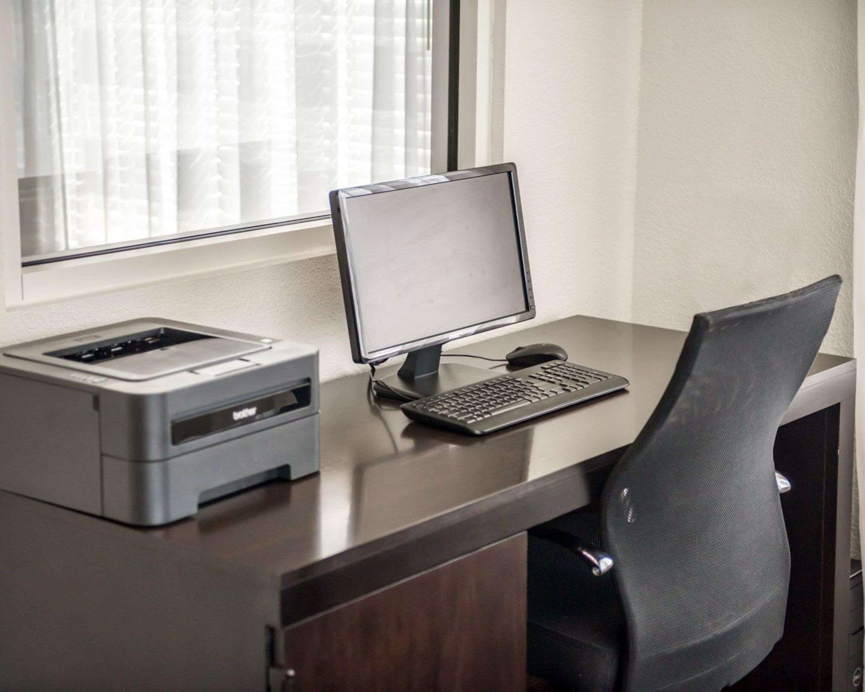 Een bureau met een computer, een printer en een zwarte kantoork stoel.