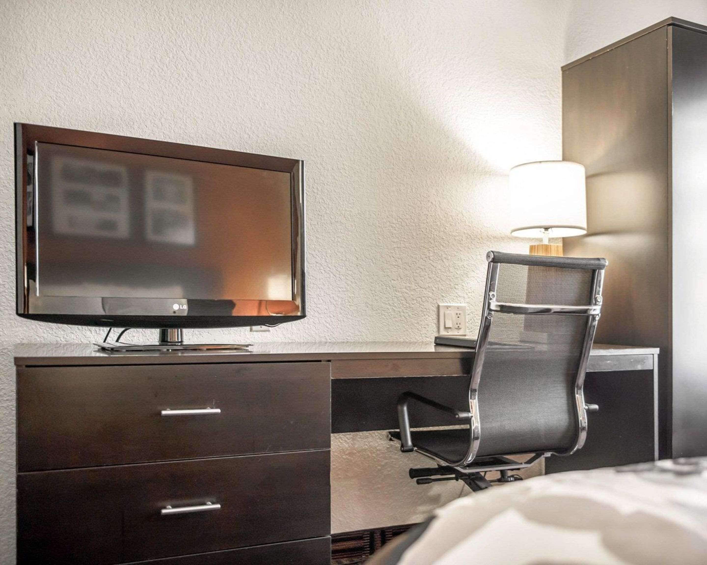 Hotellihuone, jossa on taulutelevisio, työpöytä lampun kanssa, tuoli ja vaatekaappi.
