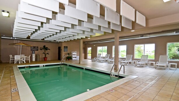 An indoor swimming pool with a tiled floor, a pool ladder, and lounge chairs arranged around the pool area. - Sleep Inn O'Fallon near I-64 (O'Fallon)