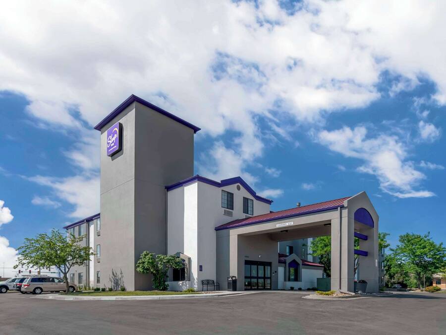 Um hotel moderno com uma torre imponente, entrada coberta e estacionamento.