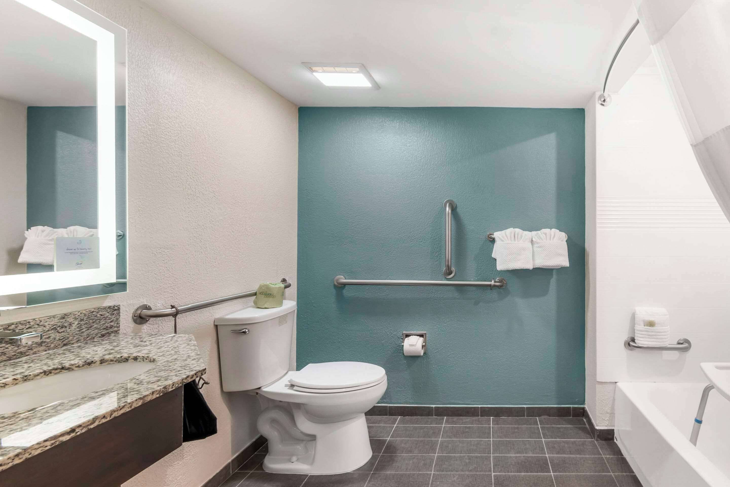 Un baño con inodoro blanco, lavabo con encimera de granito, ducha con cortina y pared color aguamarina.