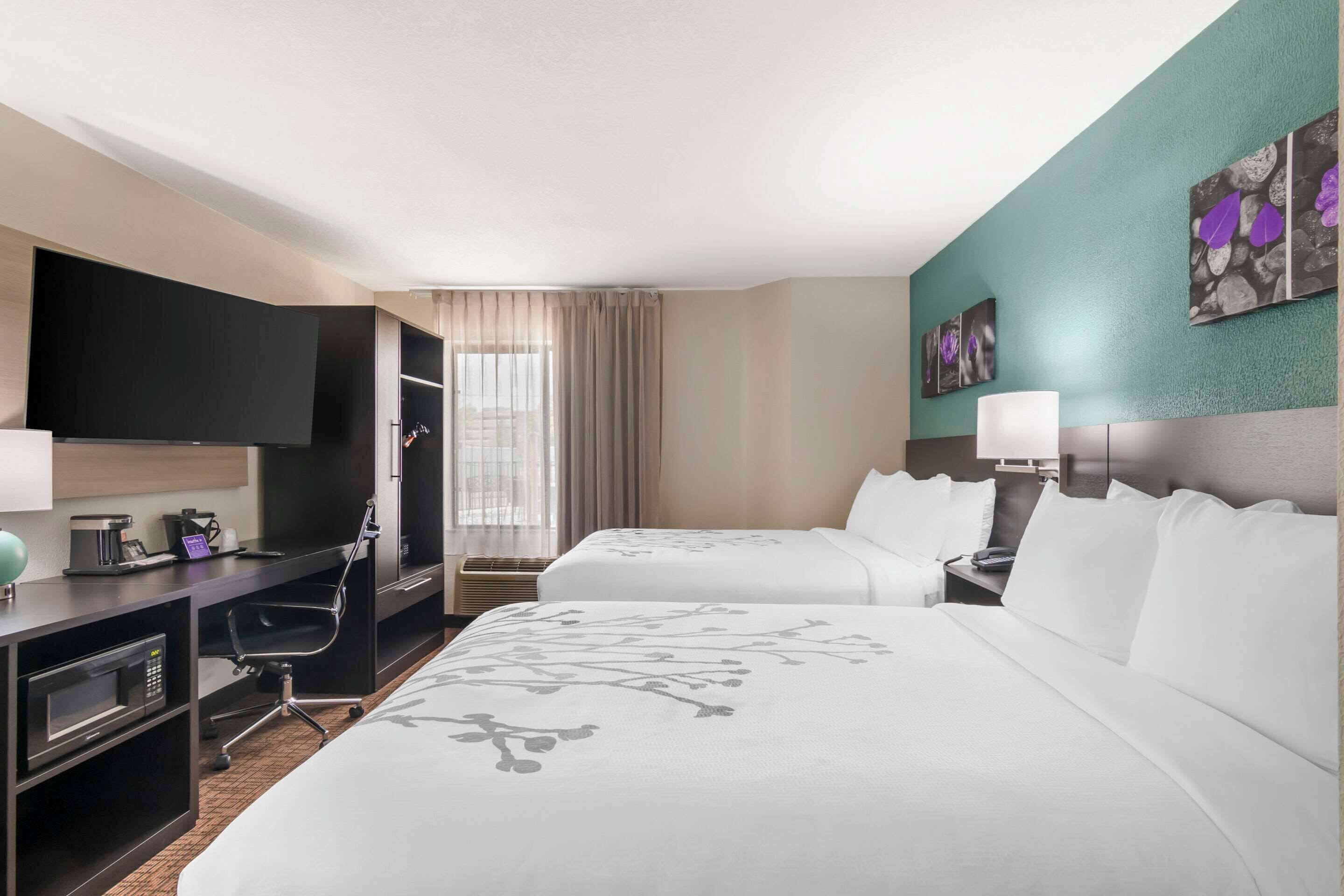 Habitación de hotel con dos camas, un escritorio con computadora, televisor y obras de arte en las paredes.