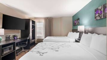 Habitación de hotel con dos camas, un escritorio con computadora, televisor y obras de arte en las paredes.