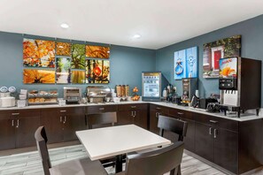 A modern kitchen with dark cabinetry, a white countertop, and a dining area with a table and chairs. - Sleep Inn Olathe - Kansas City (Olathe)