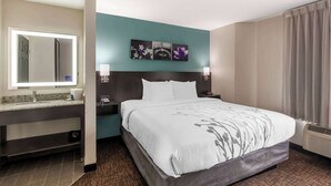 A hotel room with a bed, a nightstand, a mirror, and a wall art piece above the bed.