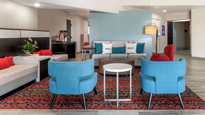 A modern living room with a sofa, two blue armchairs, a coffee table, and a patterned rug.