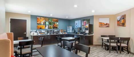 A modern hotel room with a dining area, kitchenette, and artwork on the walls.