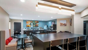 A modern kitchen with a central island, a dining area with a long table and chairs, and a sofa with red cushions. - Sleep Inn Olathe - Kansas City (Olathe)