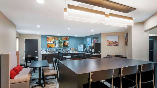 A modern kitchen with a central island, a dining area with a long table and chairs, and a sofa with red cushions.