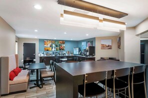 Una cocina moderna con una isla central, un área de comedor con una mesa larga y sillas, y un sofá con cojines rojos.