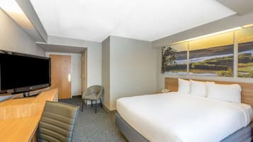 Habitación de hotel con una cama grande, un escritorio, un televisor de pantalla plana, una silla y un cuadro de un paisaje en la pared.