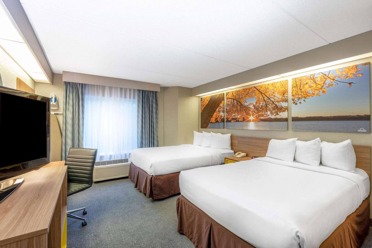 Habitación de hotel con dos camas, un escritorio con televisor y un ventanal con cortinas.