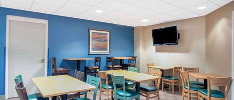 A conference room with multiple tables and chairs, a door, a framed artwork on the wall, and a mounted TV.