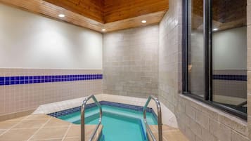 A swimming pool with a tiled border and metal ladder, surrounded by beige and blue tiles, with wooden ceiling beams and a brick wall.