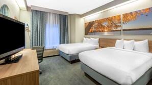 Hotellihuone, jossa on kaksi sänkyä, televisio, työpöytä ja suuri ikkuna, jossa on verhot.