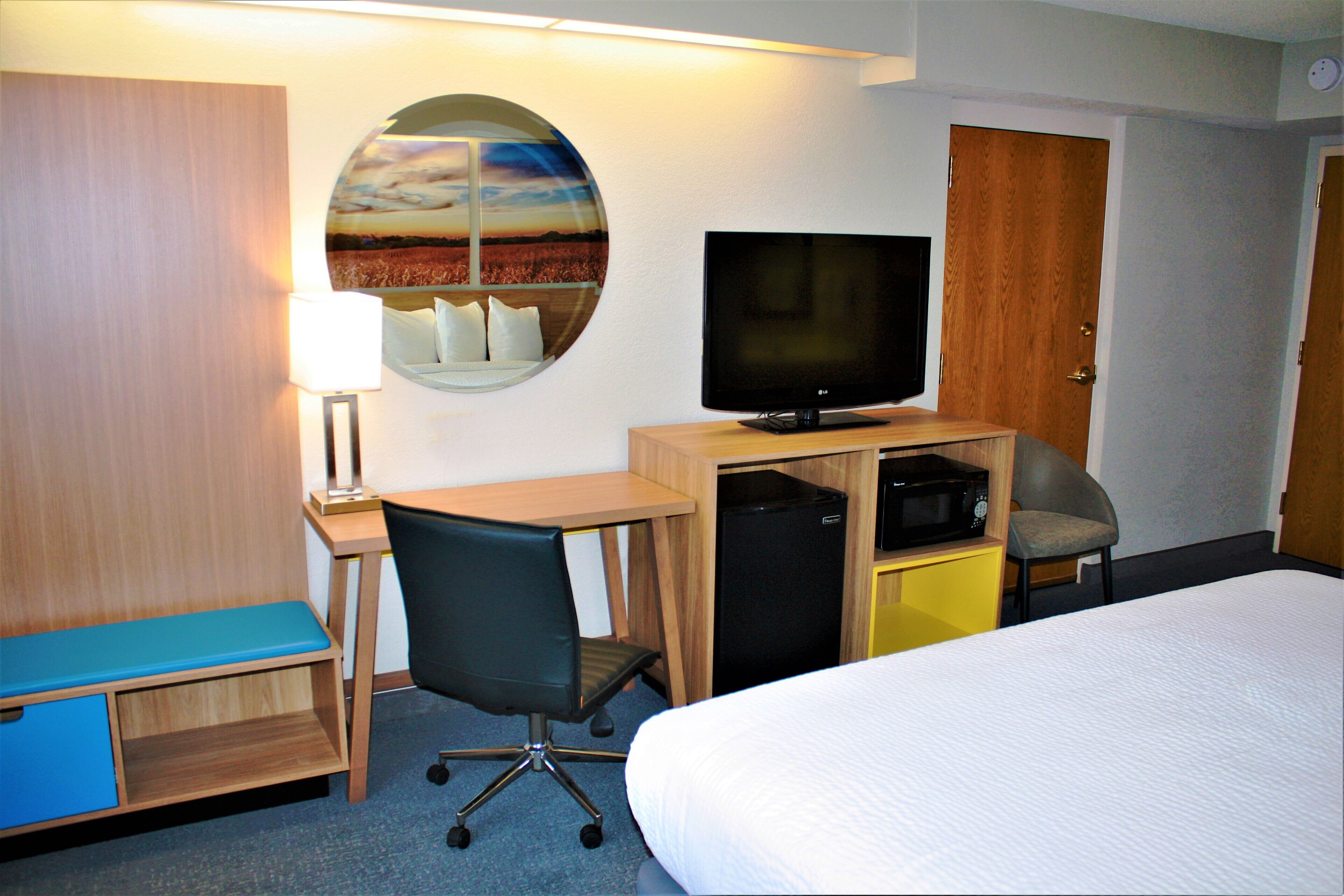 A hotel room with a bed, desk, chair, television, and a circular mirror on the wall.
