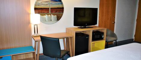 A hotel room with a bed, desk, chair, television, and a circular mirror on the wall.
