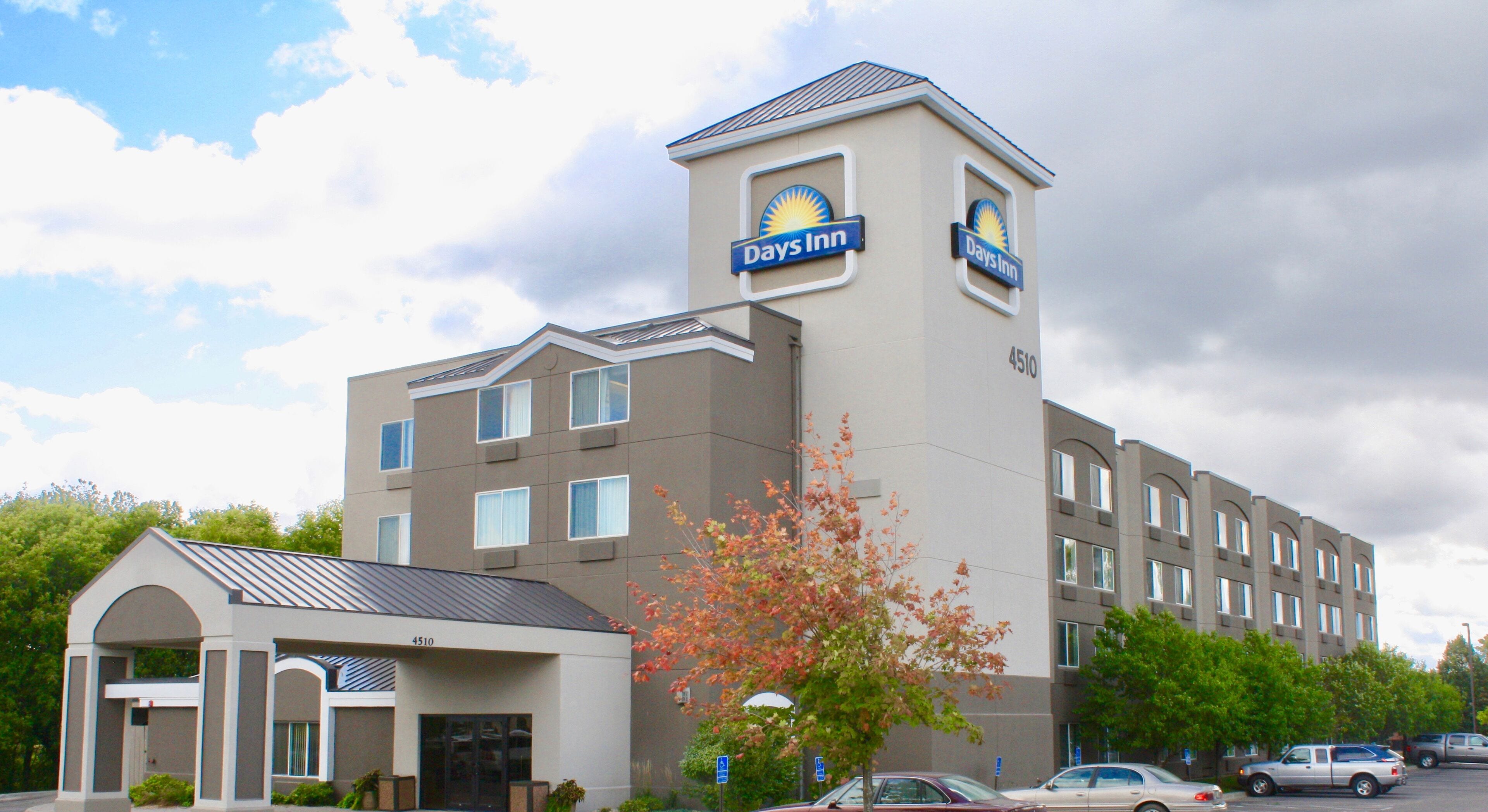 Un hotel Days Inn con un diseño moderno, que presenta una torre destacada con el logotipo del hotel, múltiples ventanas y un estacionamiento con coches.