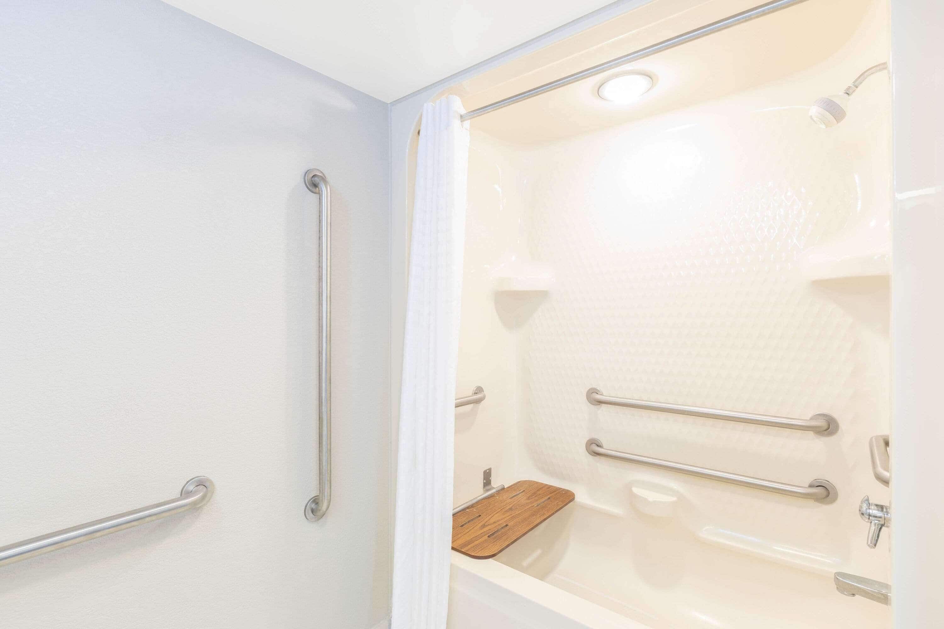 A bathroom with a bathtub, grab bars, and a wooden bath mat.