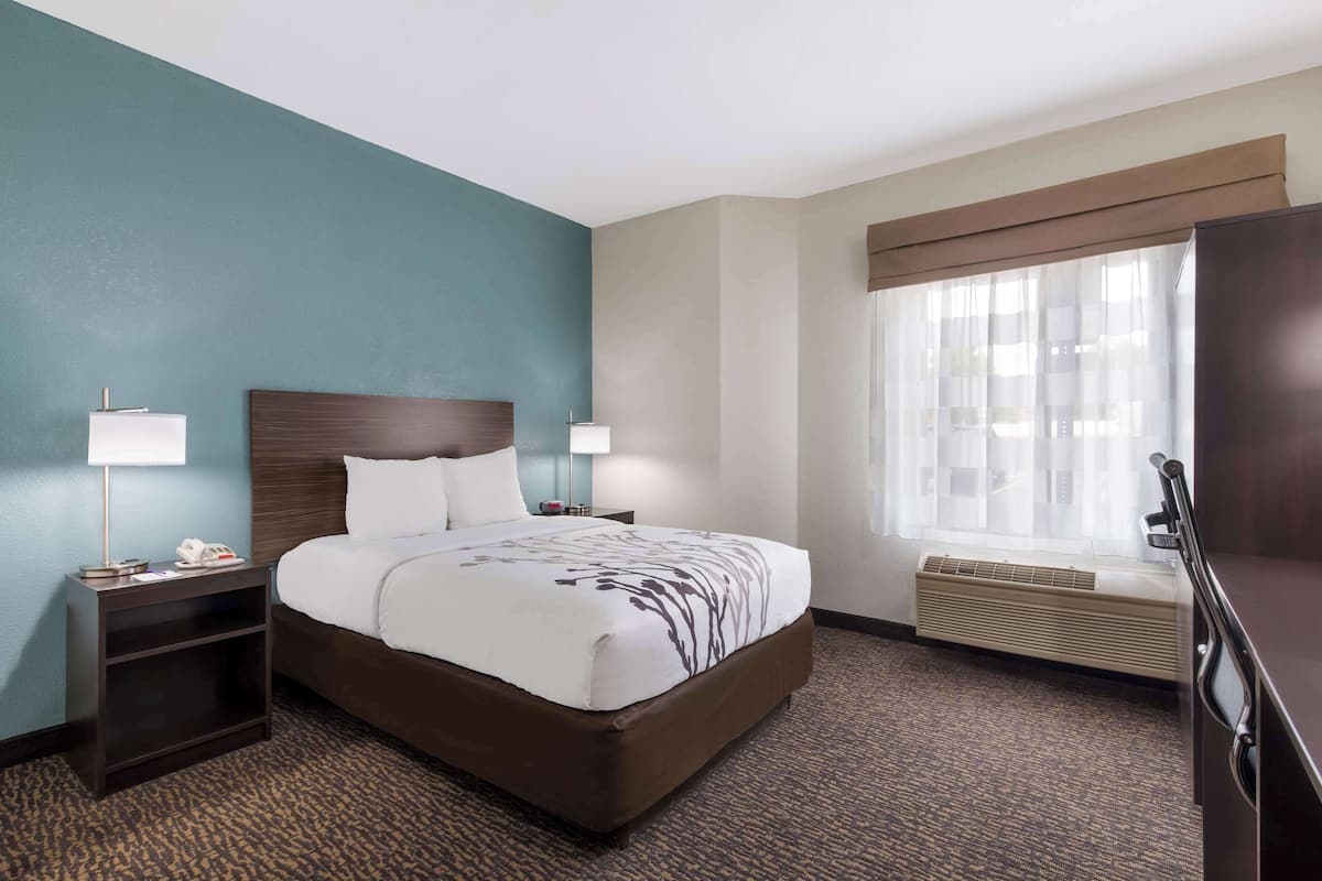 A hotel room with a bed, bedside tables, a lamp, a heater, and a window with curtains.